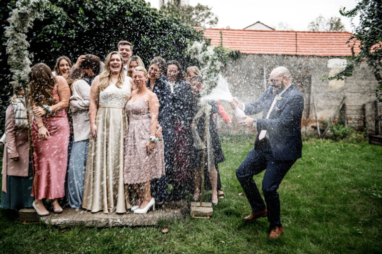 Ausgelassene Stimmung – Ein Gast sprüht Champagner während des Gruppenfotos bei der Hochzeit